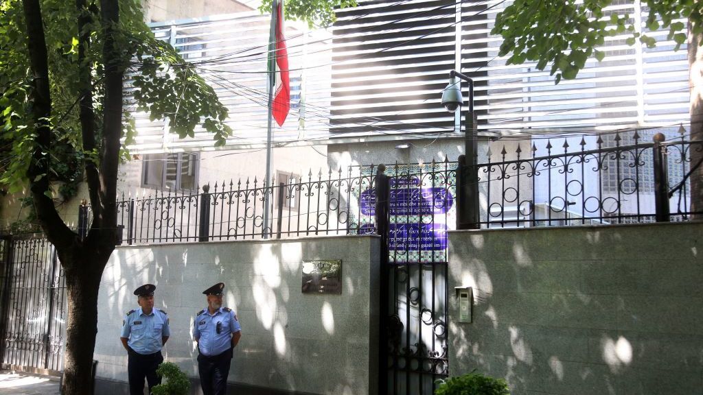 Two security guards stand outside the walls of the Iranian embassy in Tirana, as an Iranian flag looms over them