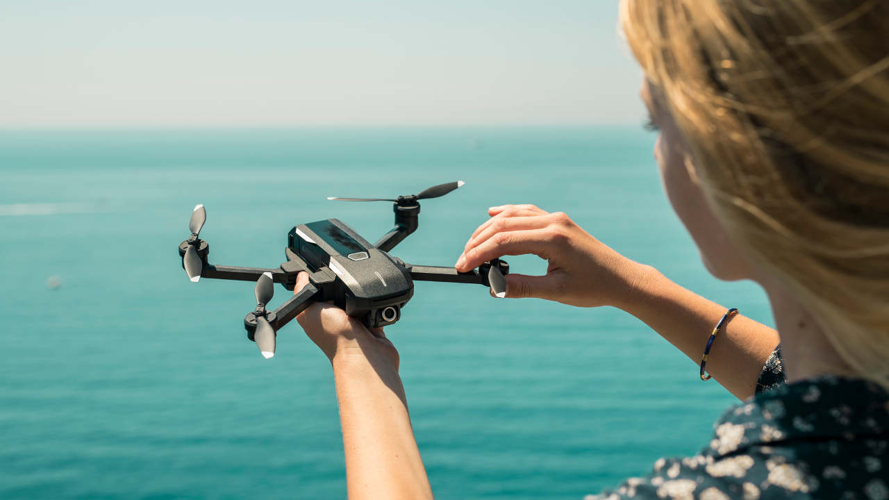 Woman standing near a large body of water holds the Mantis Q drone. 