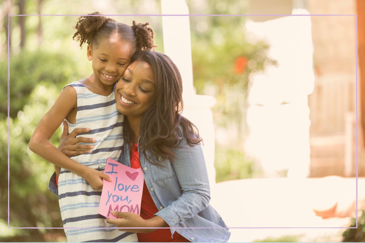 A woman and young girl hugging and holding a homemade Mother&#039;s Day card