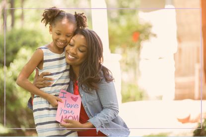 A woman and young girl hugging and holding a homemade Mother's Day card