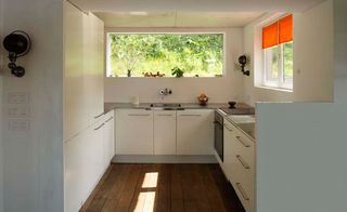 Kitchen room interior in the VW House by Franklin Azzi, white units, wooden worktop, white walls, windows, black hob and oven, outside view of garden shrubs