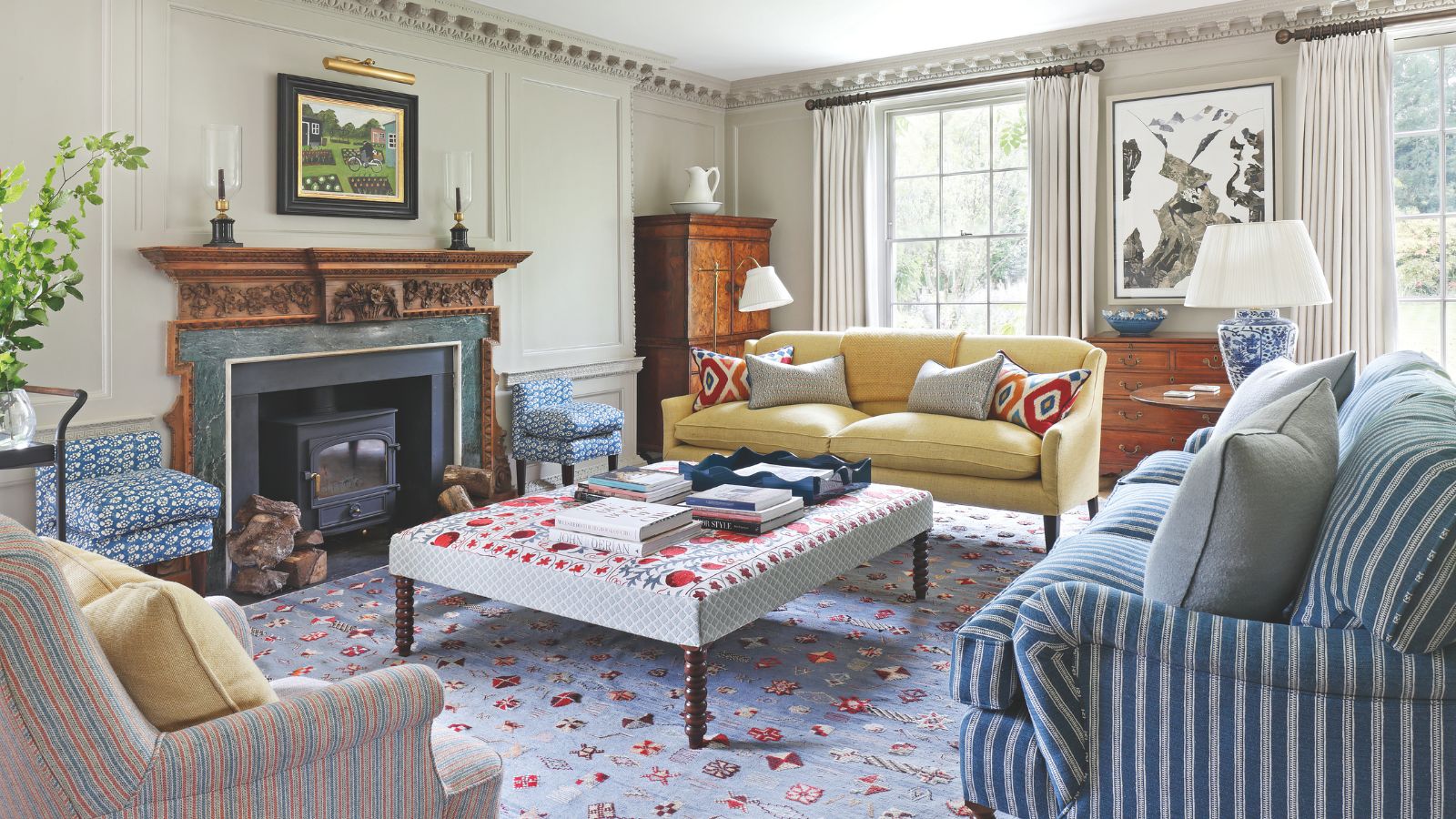 Traditional living room with large windows a yellow couch and striped couches positioned around a upholstered coffee table