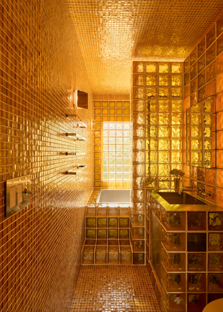 A yellow toned bathroom with floor to ceiling golden tiles and yellow glass blocks