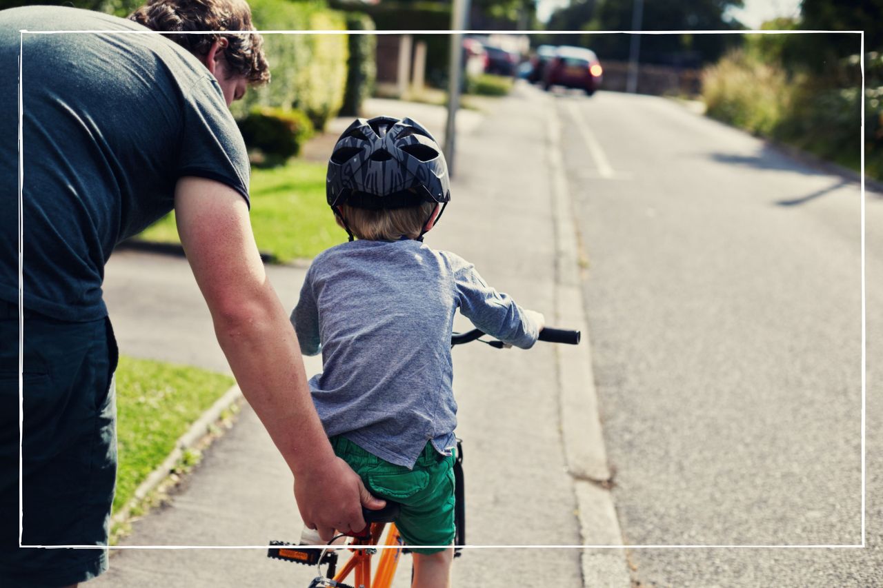 Father holding on to bike seat to steady the bike, while his helmet-wearing child learns to ride