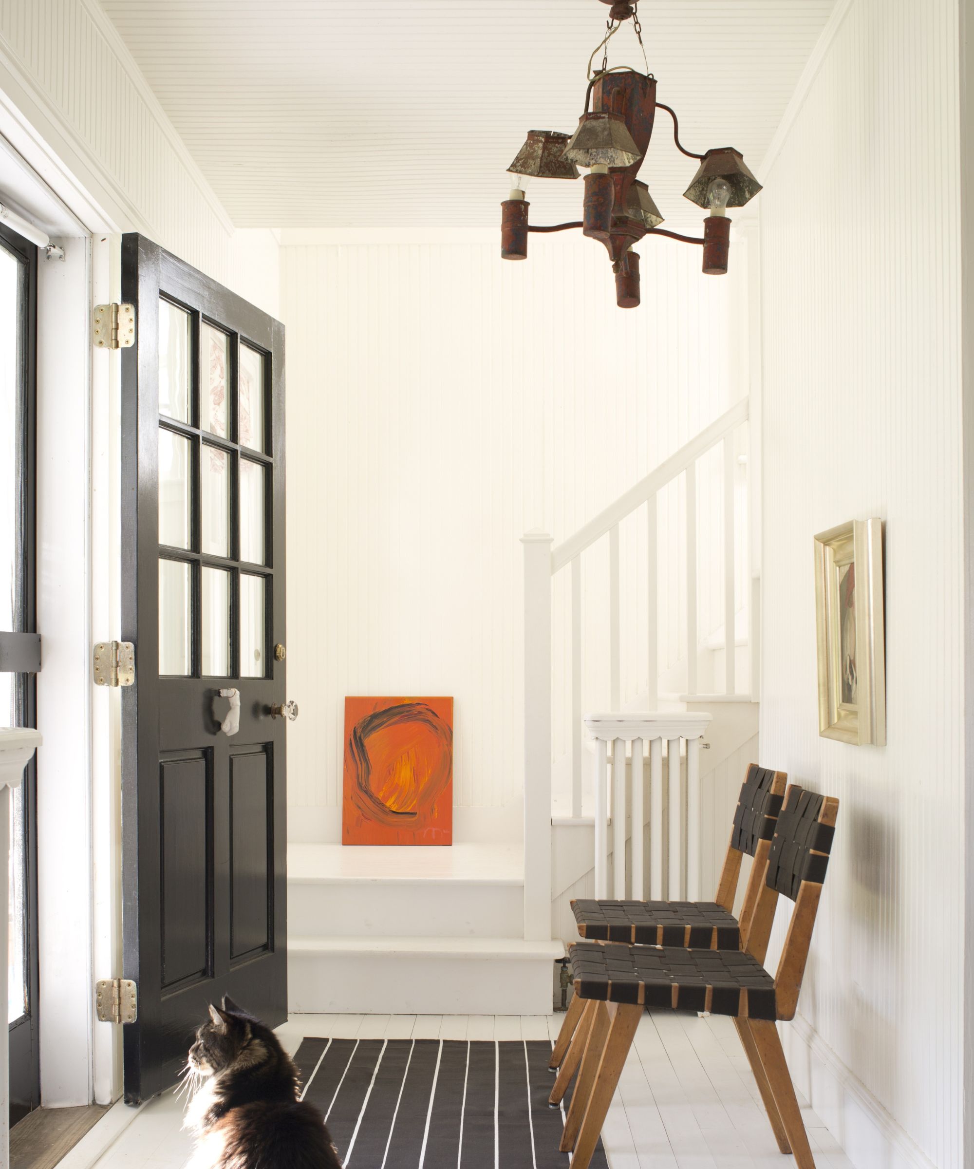 White entryway with black front door and black striped run with wooden and black chairs and a cat