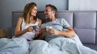 A couple smile while drinking coffee in bed