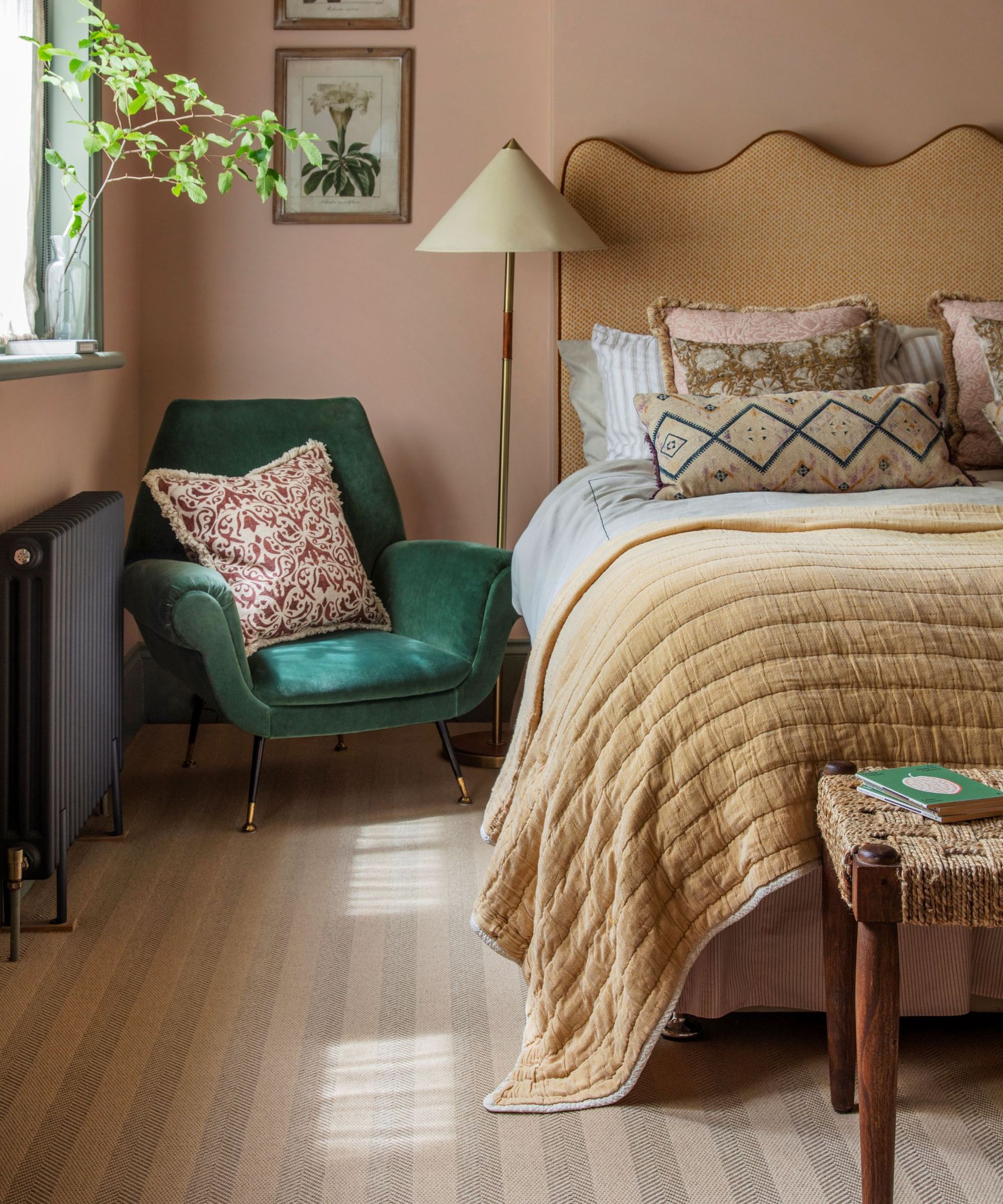 Bedroom with pastel pink walls, yellow headboard and green velvet armchair and striped carpet