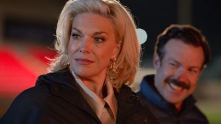 Hannah Waddingham as Rebecca looking to her right with Ted Lasso smiling in the background standing behind her.