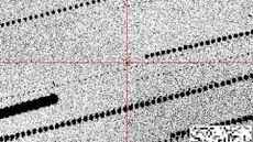 A grainy black-and-white image with a black dot in red crosshairs in the center