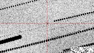 A grainy black-and-white image with a black dot in red crosshairs in the center