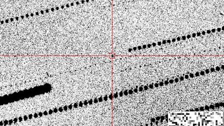 A grainy black-and-white image with a black dot in red crosshairs in the center