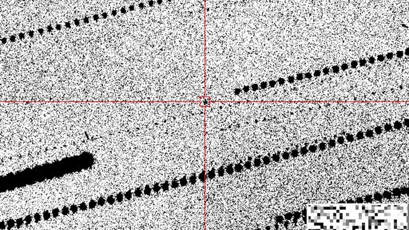 A grainy black-and-white image with a black dot in red crosshairs in the center