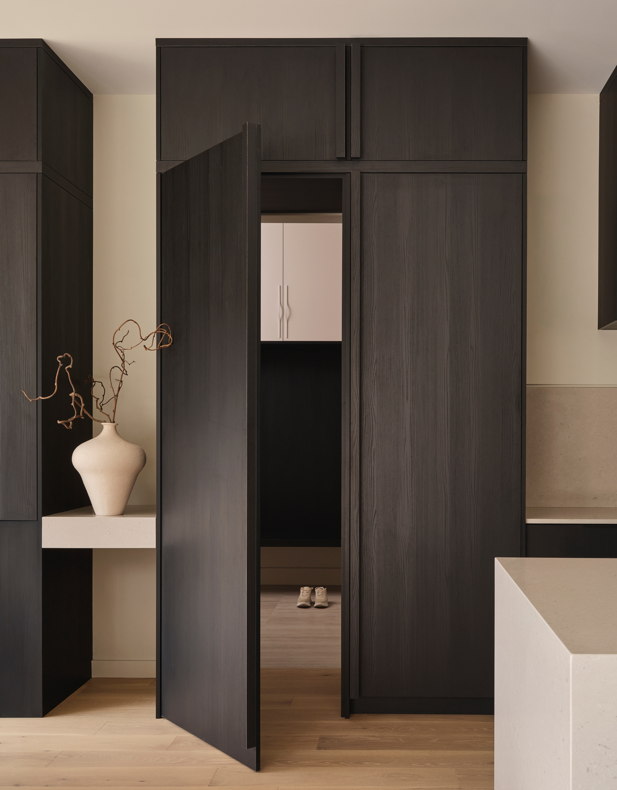 A minimalist kitchen-side space with dark wood cupboards, an off-white vase, and stone counters