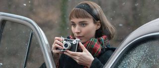 Rooney Mara standing next to a car, holding an Argus C3