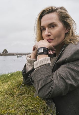 Kate Winslet posing wearing a Longines Mini DolceVita watch with black double straps with the ocean in the background.