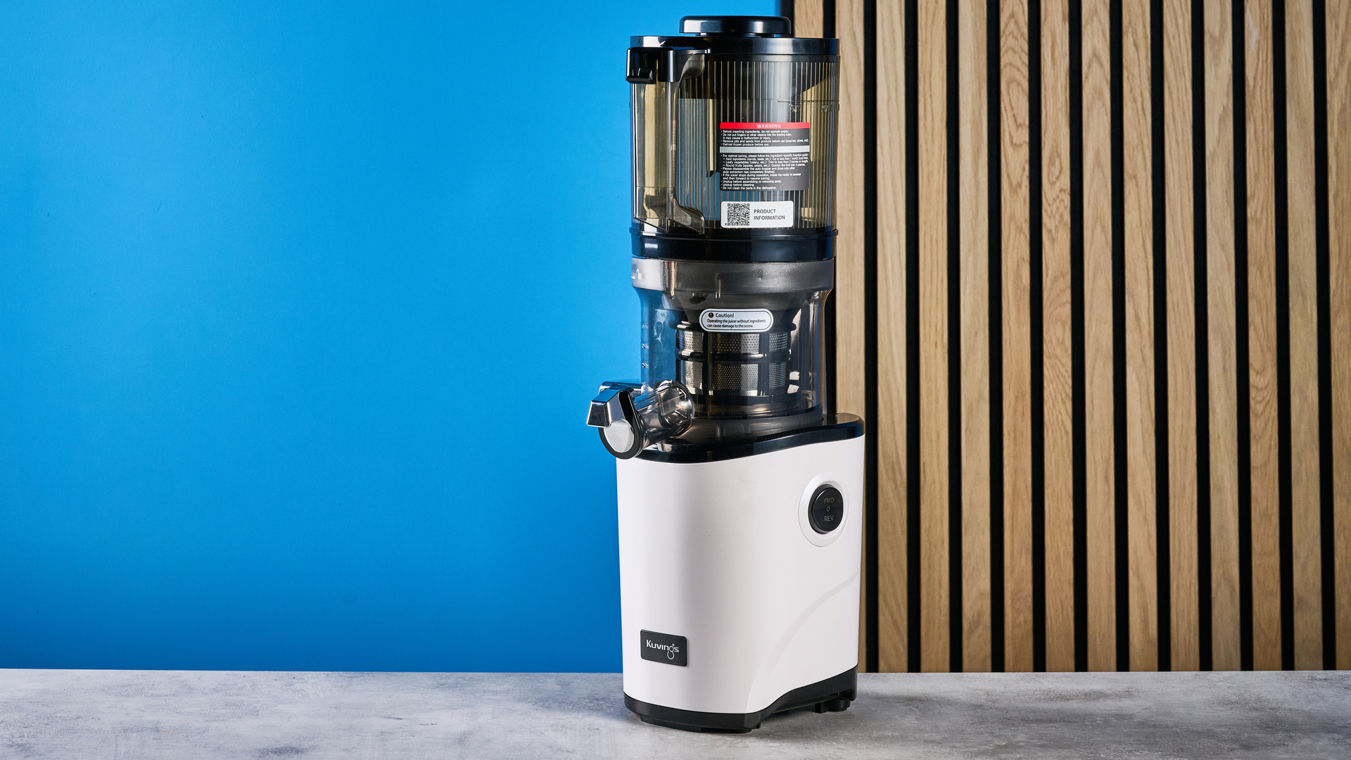 Kuvings Auto8 hands-free slow juicer photographed on a blue background.