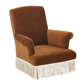 Burnt orange, velvet accent chair with cream fringe around the bottom