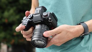 Panasonic Lumix GH7 held in the hands of a person wearing a green t-shirt