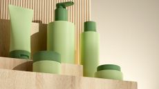 Green cosmetic bottles and containers displayed on a tiered wooden platform.