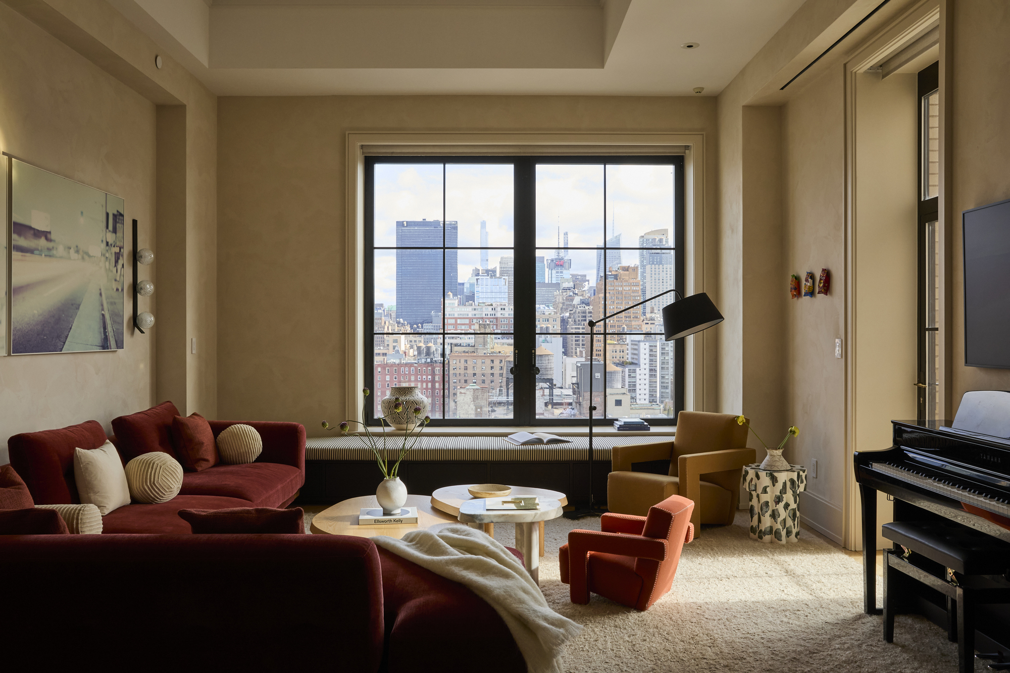 A living room with cream walls, a red sofa, and an orange accent chair next to a coffee table
