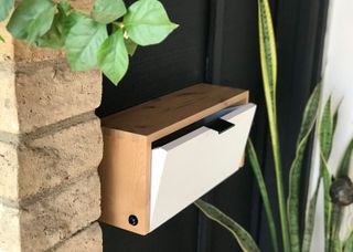 Homemade wooden mailbox on a black wall.