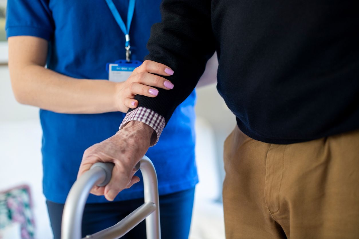 Nursing home aide walks with elderly man.