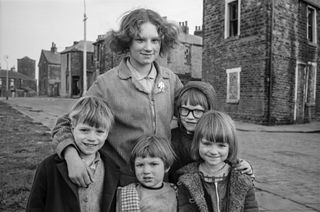 Black and white photograph of a young woman with her arms around four small children - all smiling at the camera.