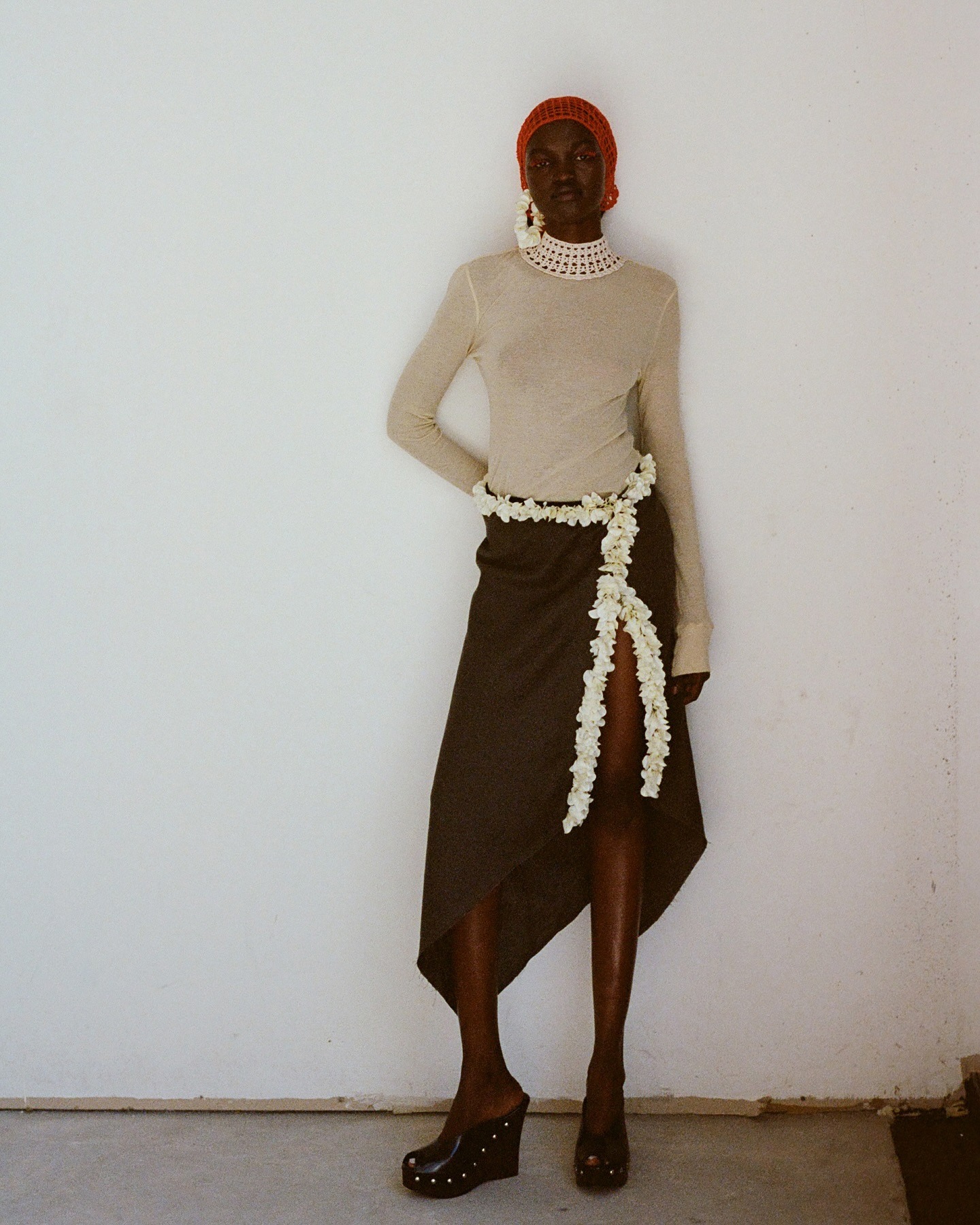 a woman wears a red crochet hat, ivory long sleeve, brown skirt, and clogs.