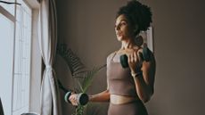 Woman in tank top lifting dumbbells at home