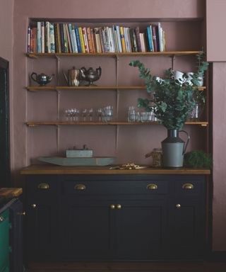 dusky pink and navy kitchen with shelving in the an alcove, navy blue cabinet, wood countertop, vase of eucalyptus