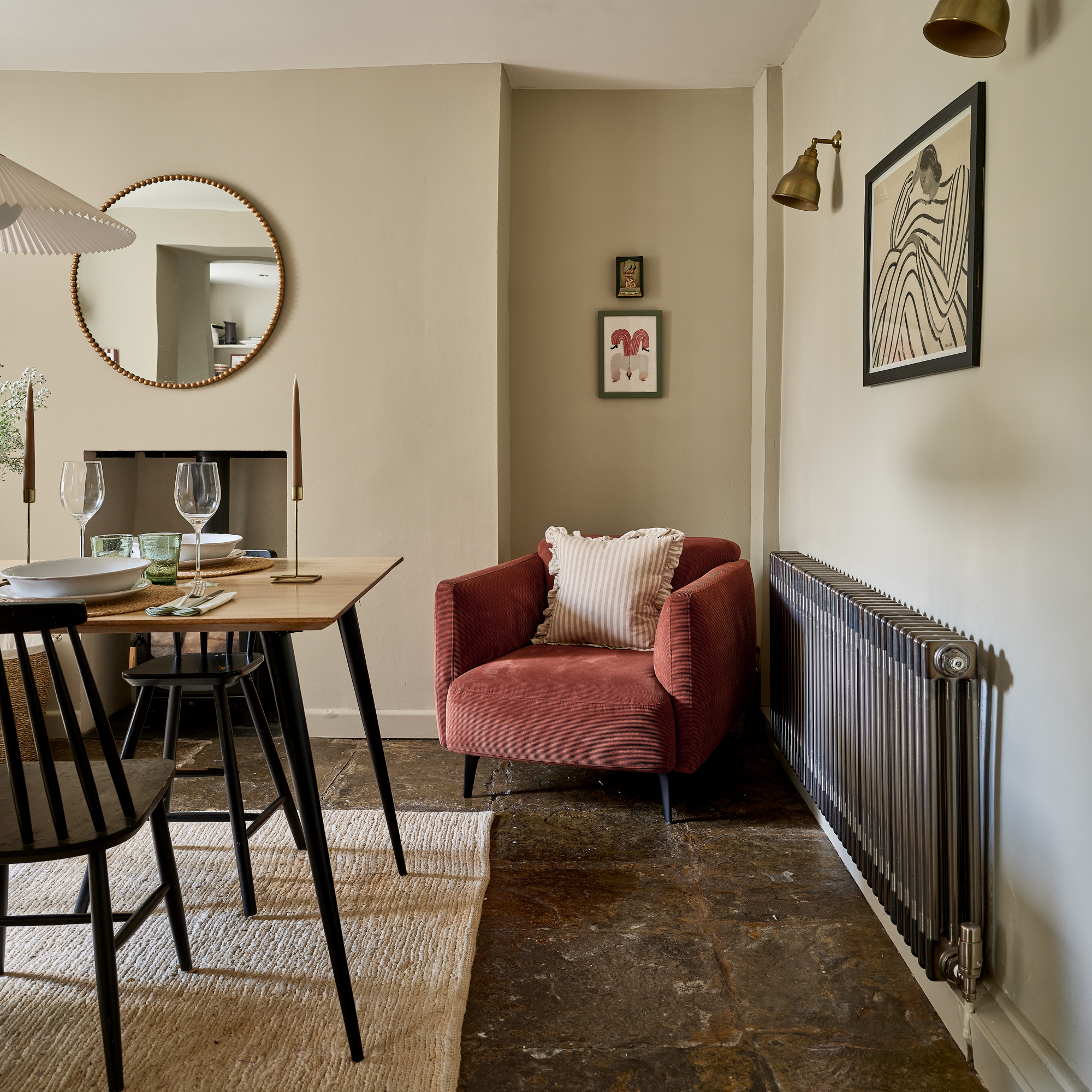 a neutral dining room with a painted black wooden table and chairs slate flooring traditional radiator and a terracotta velvet upholstered armchair