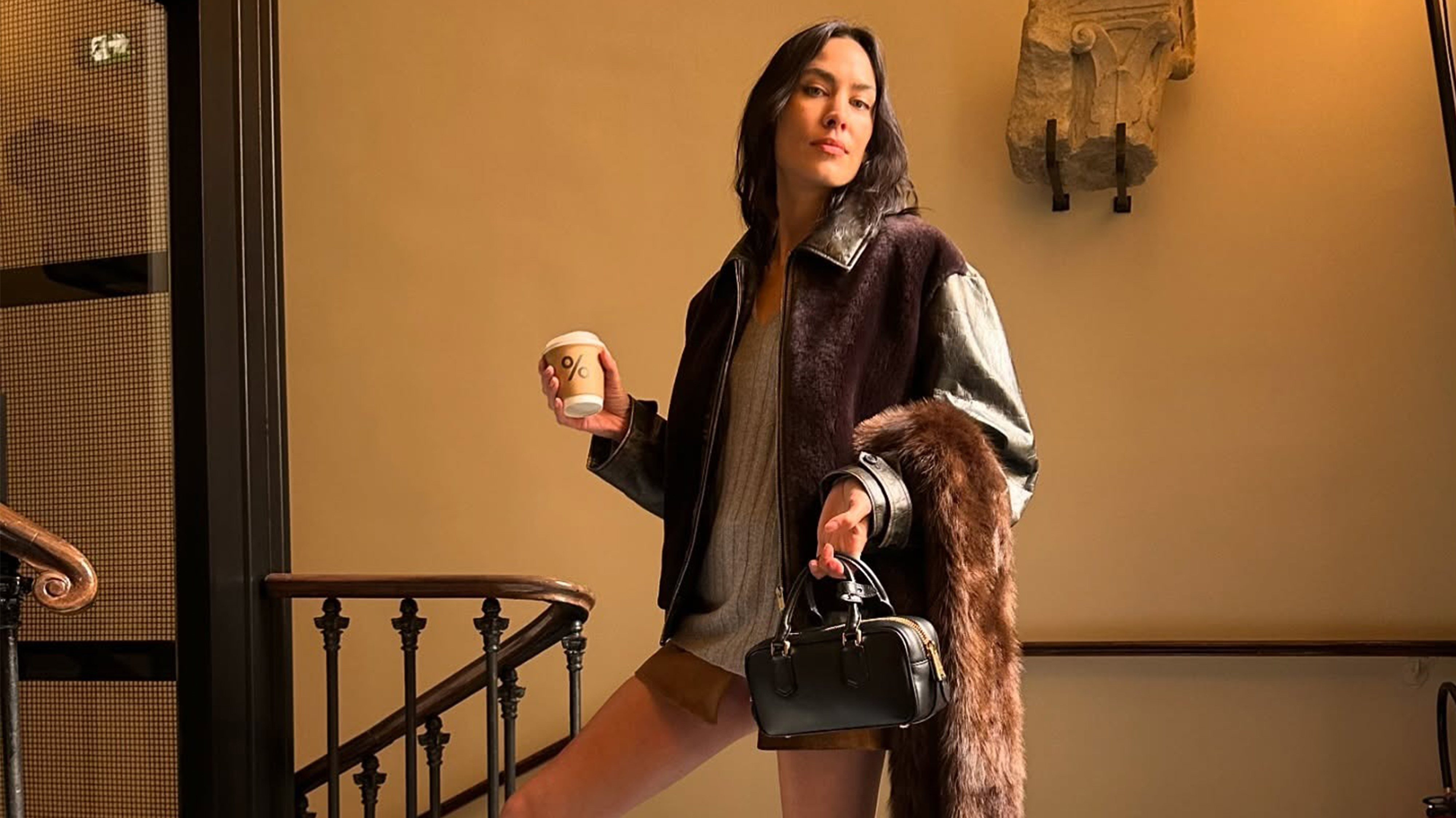 Alexa Chung before the Miu Miu fashion show as part of Spring/Summer 2026 Paris Fashion Week. She&#039;s wearing a fur and leather jacket, a gray sweater, a brown suede skirt, and carrying a black bag.