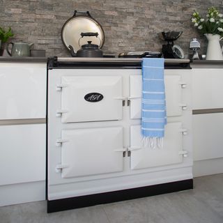 White aga in a kitchen with white cabinets and stone wall tiles
