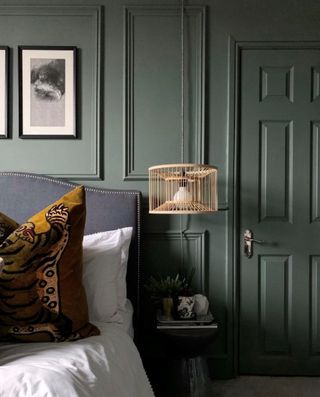 A green paneled bedroom with pendant side lamp and framed monochrome wall art