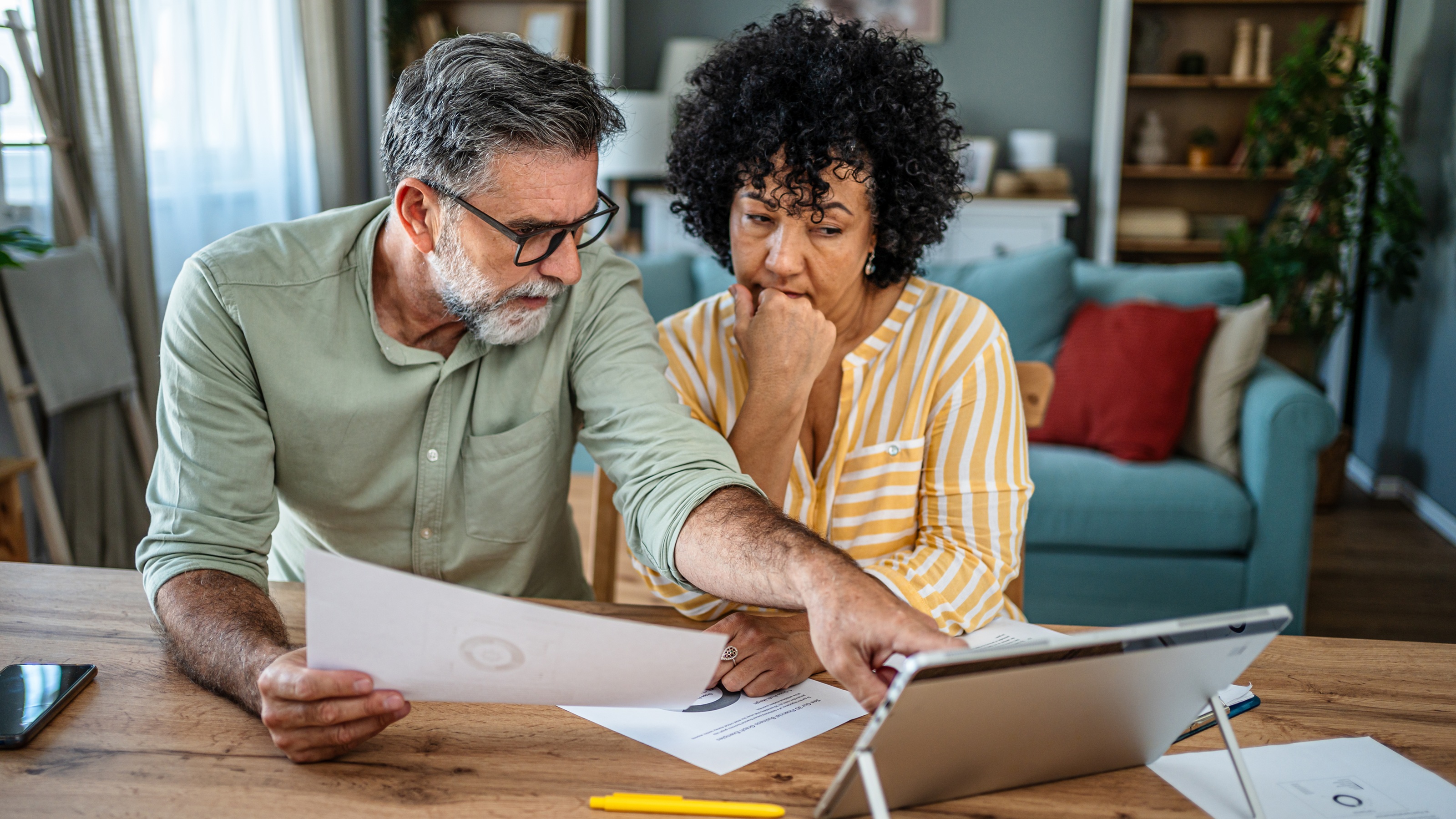 An older couple look over financial information on a laptop at their dining room table.