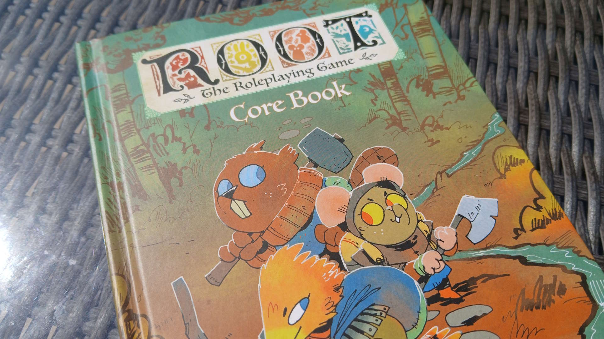 Root: The Roleplaying Game Core Book on a gray wicker surface