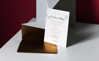 Trapezoidal gold paper unfolded to reveal a gold foil-embossed invitation on white card