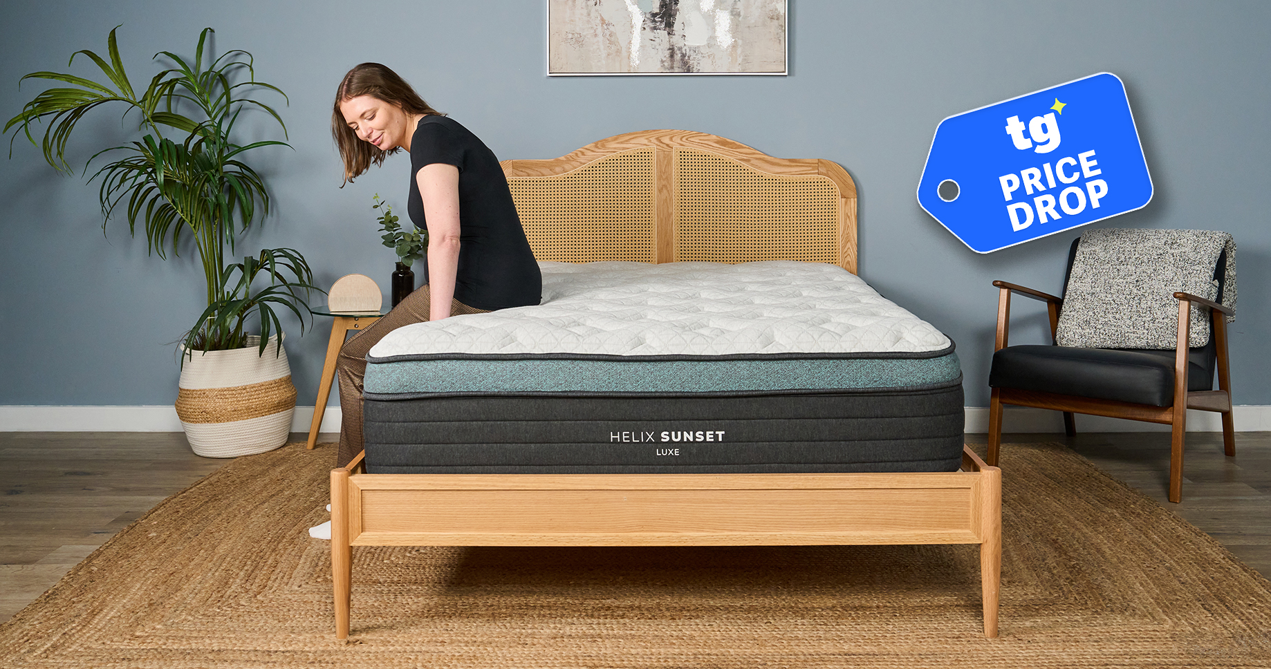 Mattress tester Ruth Jones sits on the edge of the Helix Sunset Luxe mattress on a bed frame in the Tom's Guide Sleep Lab. A Tom's Guide Price Drop deals graphic in the top right corner