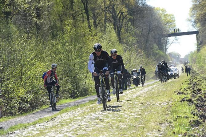 A mountain biker is passed by the Trek team in the Arenberg forest