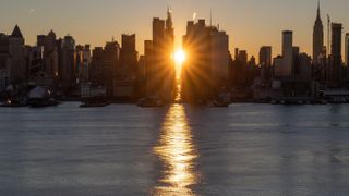 The sun rises above 42nd Street during a reverse 'Manhattanhenge' in New York, New York photographed from Weehawken, New Jersey on November 24, 2021. - 'Manhattanhenge' is a phenomenon during which the setting sun or the rising sun is aligned with the eastwest streets of the main street grid of Manhattan, New York City.