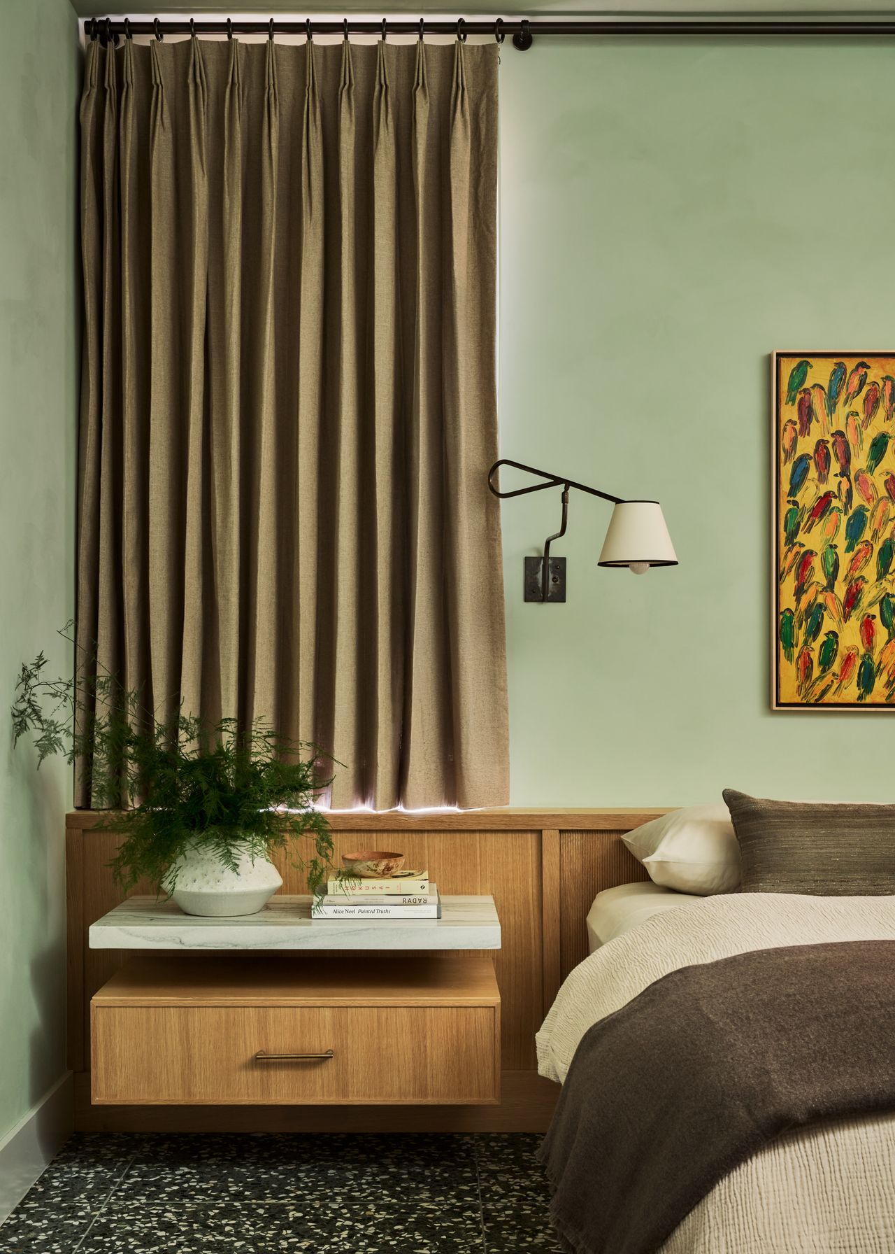 sage green bedroom with curtain over window, floating timber bedside table, artwork over bed, and wall sconce light