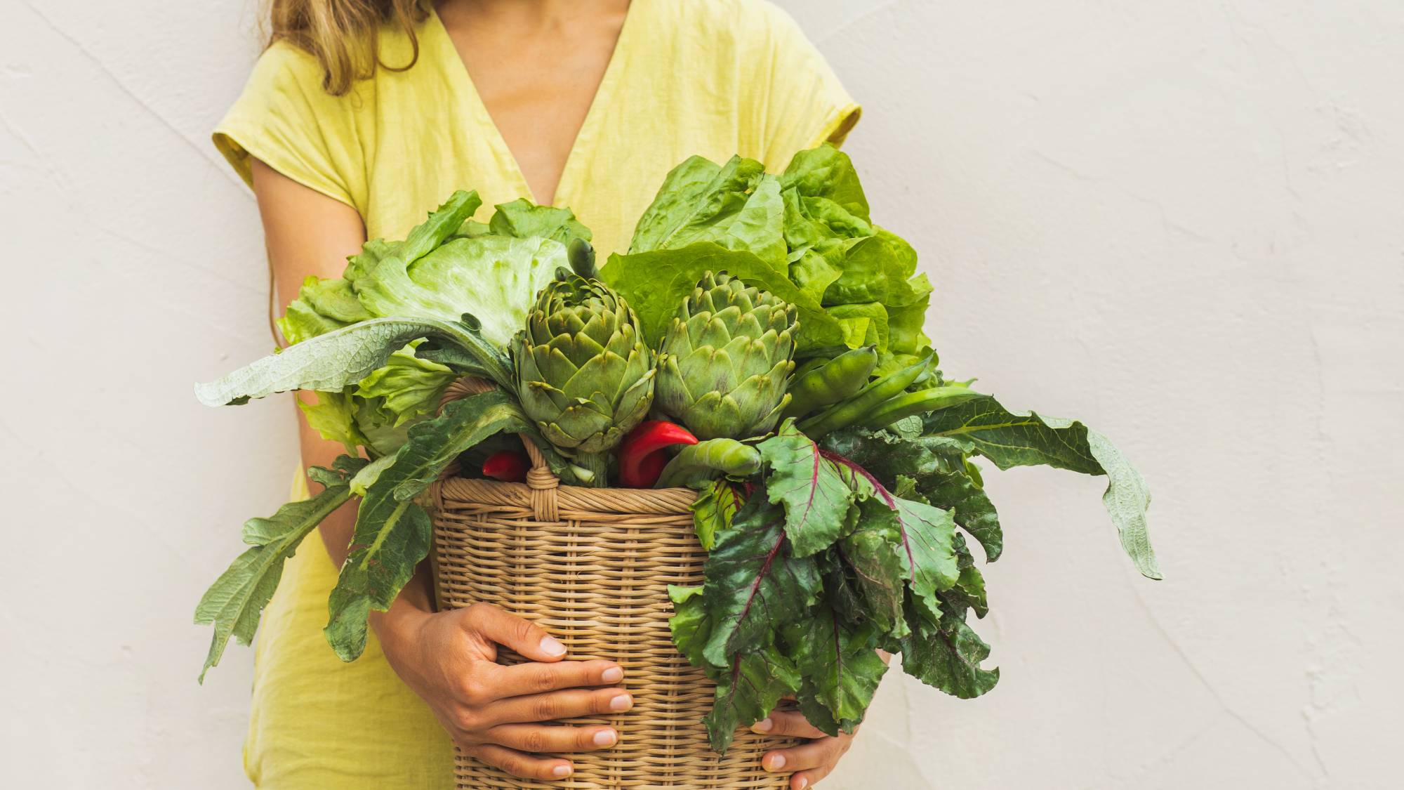 A woman's hands and torso holding a basket of fresh vegetables