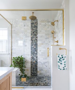 A shower with a gold border, black and white tiles, a gold shower head, and a plant inside it