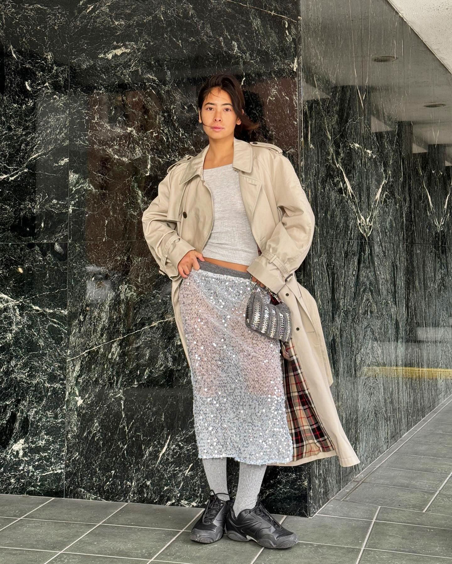 Michelle Li wearing a tan trench coat, a grey top, a grey sequin skirt, and black sneakers in NYC