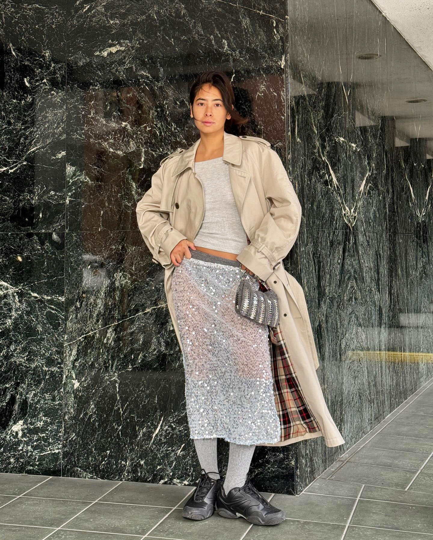 Michelle Li wearing a tan trench coat, a grey top, a grey sequin skirt, and black sneakers in NYC
