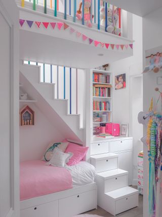 A girls white and pink bedroom featuring storage in the stairs, colour bunting and soft toys