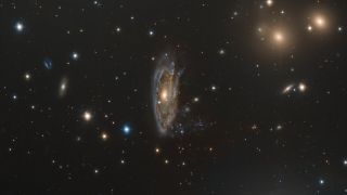 a wispy galaxy of blue and gold gasses hangs tall in space, center to many other shimmering points of light of varying sizes.