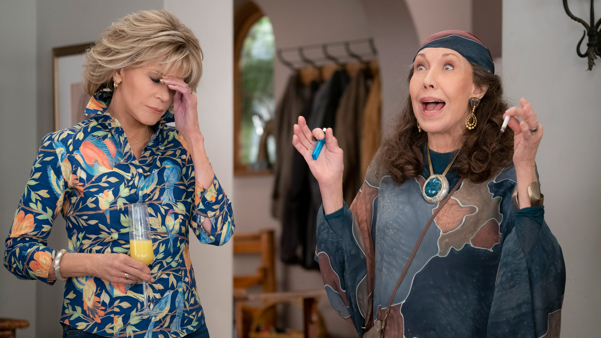 Lily Tomlin (as Frankie) holds a lighter and what appears to be a joint while Jane Fonda (as Grace) holds a hand to her own forehead