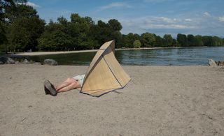 A human resting on a map and sun shield on the sand by the river. photographed during the day