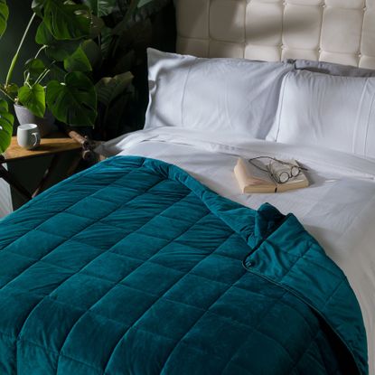 Bed with white bedlinen and teal blanket and nightstand